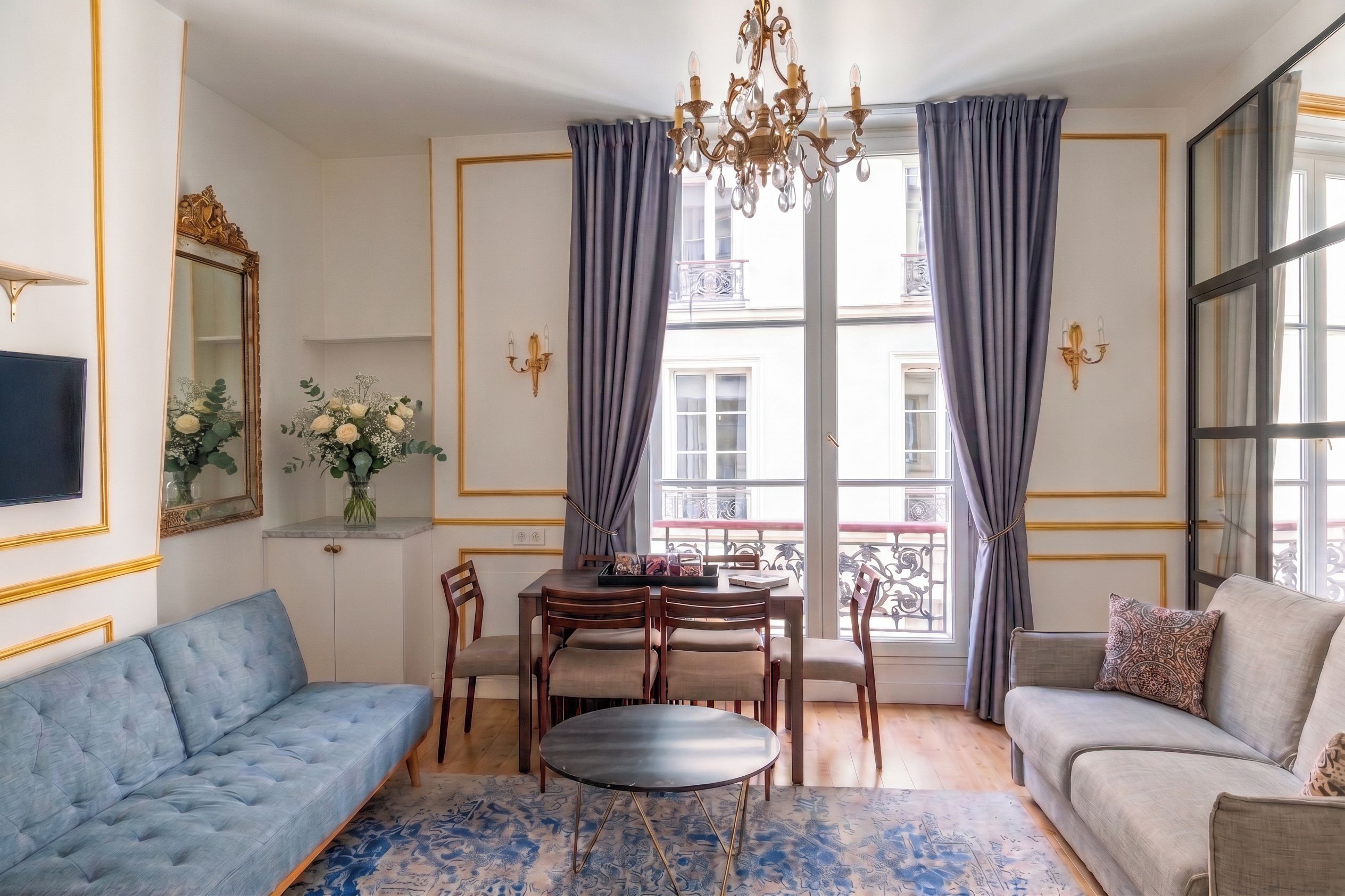 A well-lit room with a dining table, chairs, a sofa, and a chandelier.