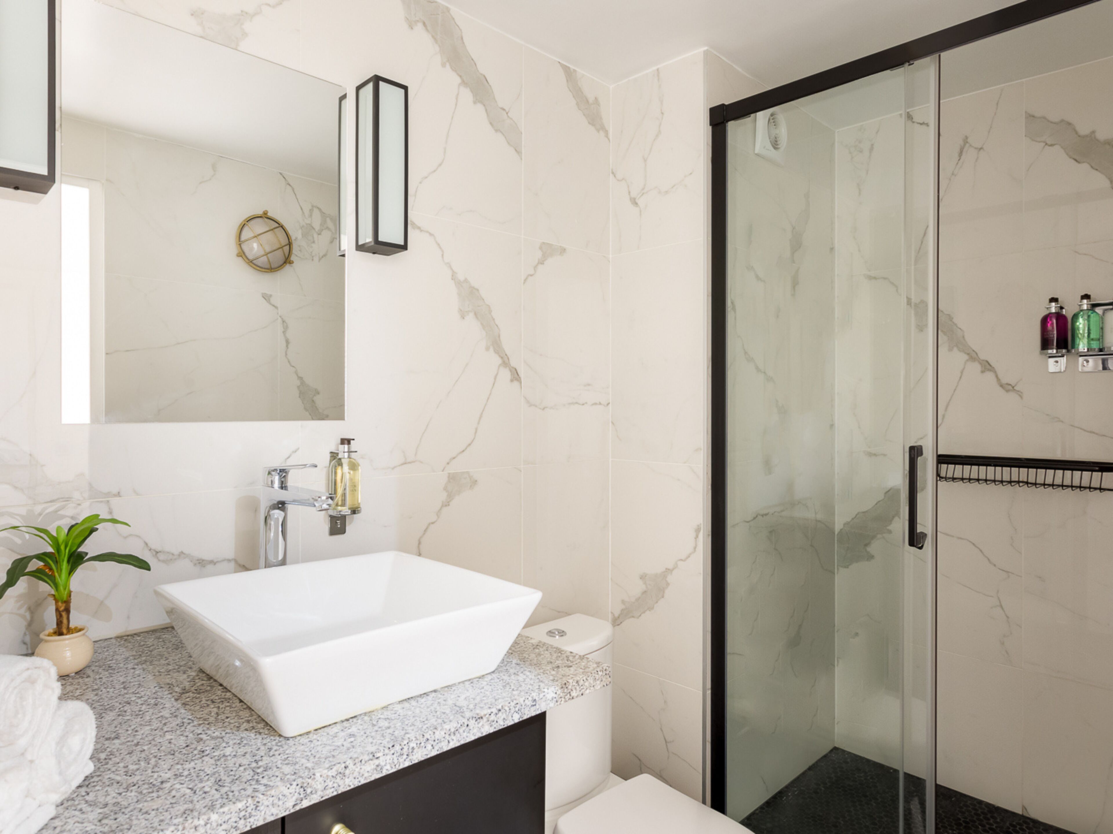 A modern bathroom with a large white sink, a glass shower enclosure, and marble walls.