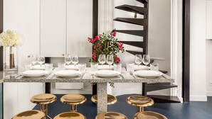 Une cuisine moderne dotée d’un îlot central, de meubles blancs, d’un escalier en colimaçon noir et d’un coin repas agrémenté d’assiettes blanches et de tabourets dorés.