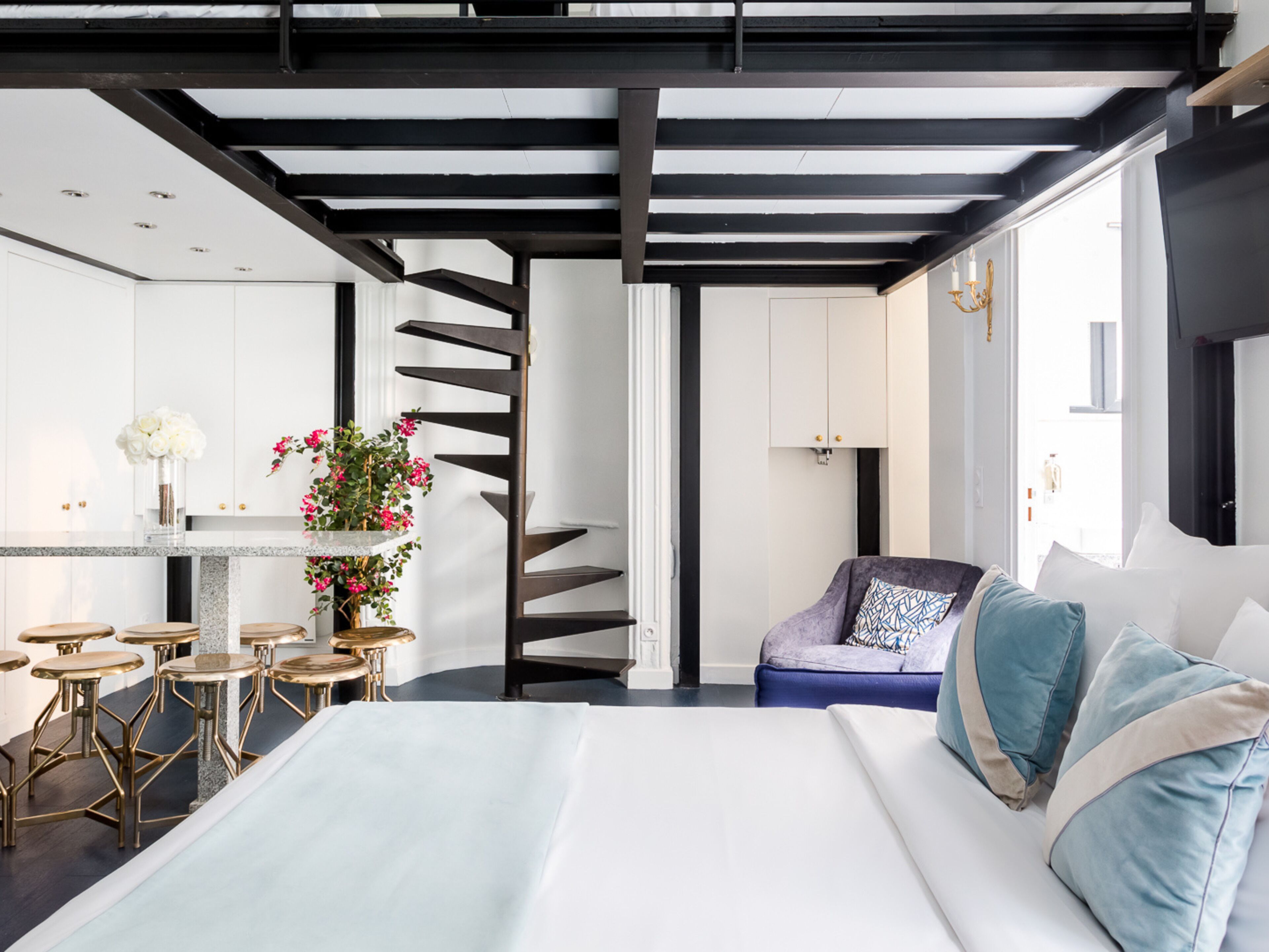 Una habitación de hotel moderna con una cama grande, un área de comedor con taburetes, una cocina y una escalera en espiral.
