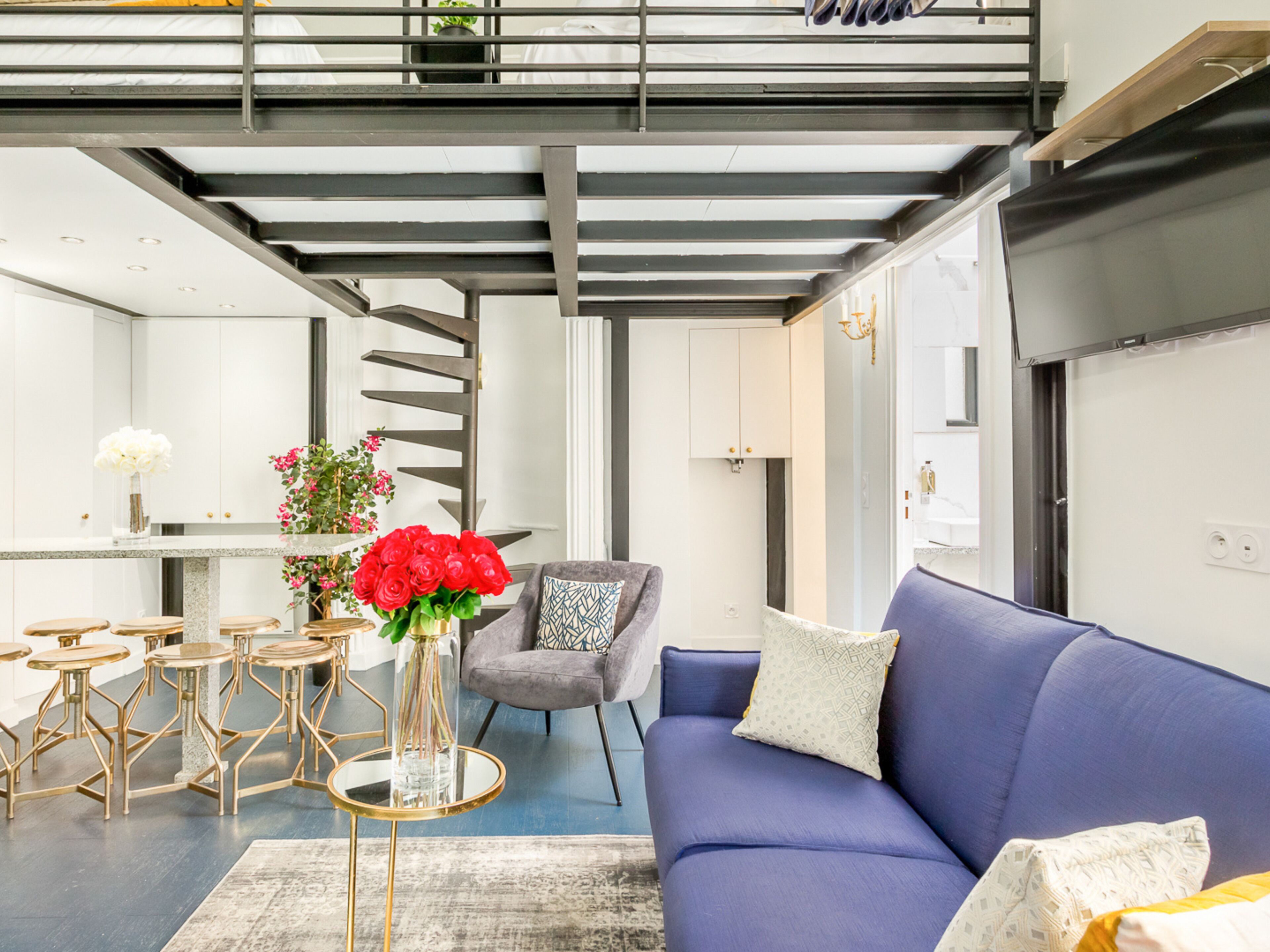 A modern living room with a blue sofa, a grey armchair, and a glass coffee table with a vase of red flowers.
