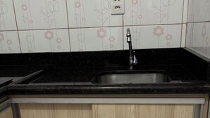 Una cocina con encimera negra, armarios de madera, pileta de acero inoxidable y un enchufe en la pared.