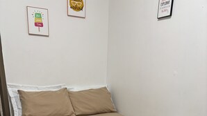 Una cama con una colcha y almohadas color crema, una manta blanca y una pared con dos cuadros enmarcados.