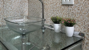 Un baño con lavamanos de cristal, un espejo redondo y una planta en maceta.