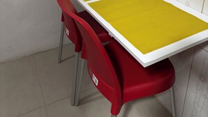 Un pequeño comedor con una mesa amarilla y sillas rojas.