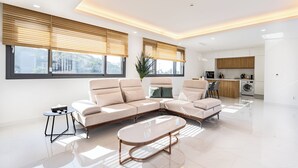 A modern living room with a sectional sofa, a round coffee table, and a kitchen area in the background. - Gobajinin Private Pool Villa (Jeju City)