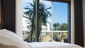 A bedroom with a large window, a bed, and a view of a stone wall and palm trees outside. - Gobajinin Private Pool Villa (Jeju City)