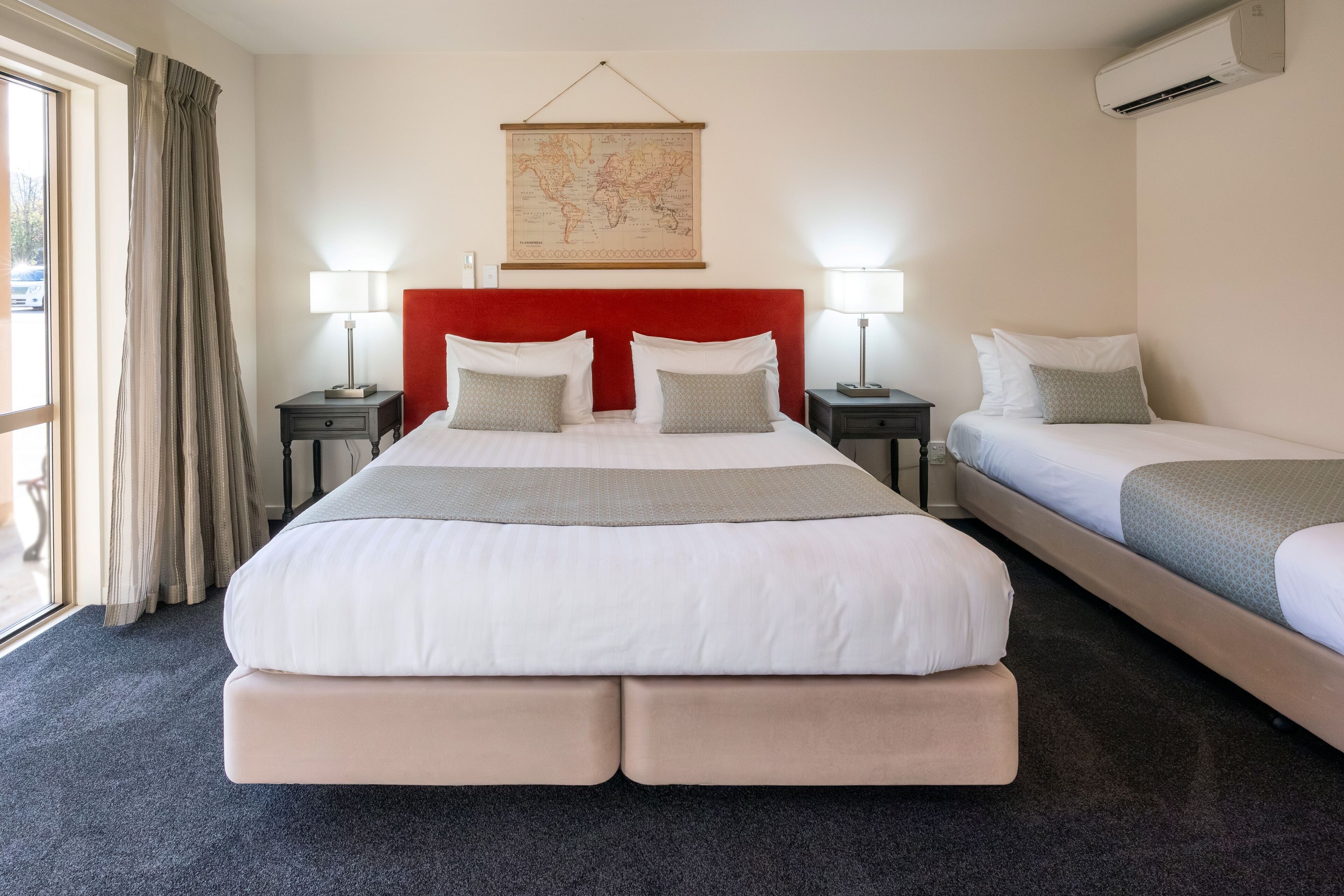 Una habitació d'hotel amb un llit gran, dues taules de nit, un mapa mundial a la paret i un aparell d'aire condicionat.