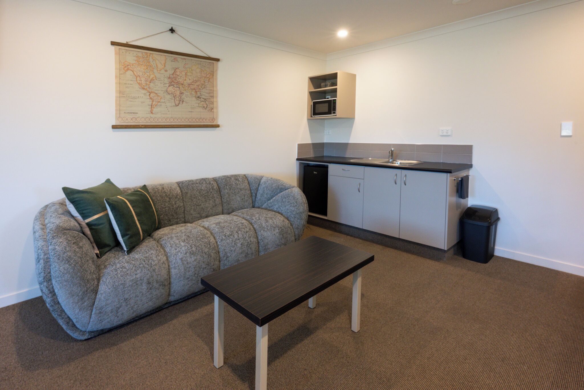 Un espacio habitable compacto con sofá, una mesita, kitchenette y un cubo de basura.
