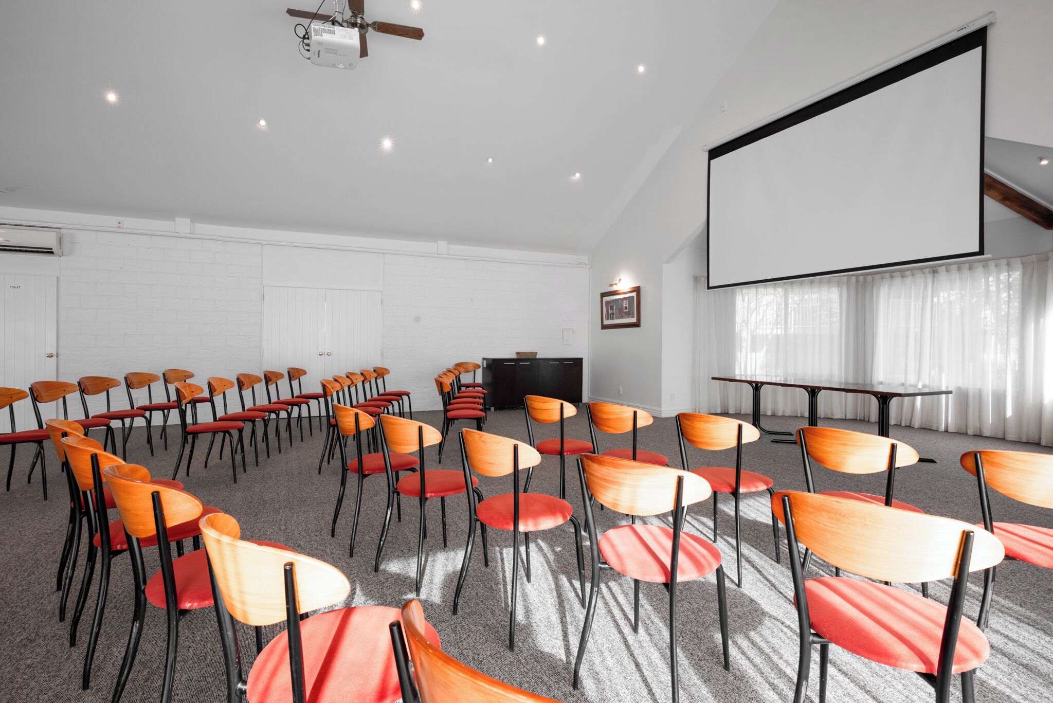 Una sala de conferències amb files de cadires, una pantalla de projector i una televisió.