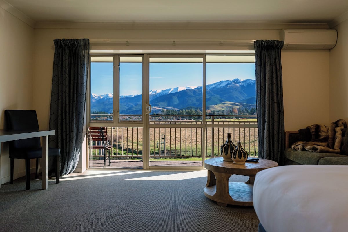 Habitación de hotel con un amplio ventanal corredero que da a un balcón con vistas a la montaña.