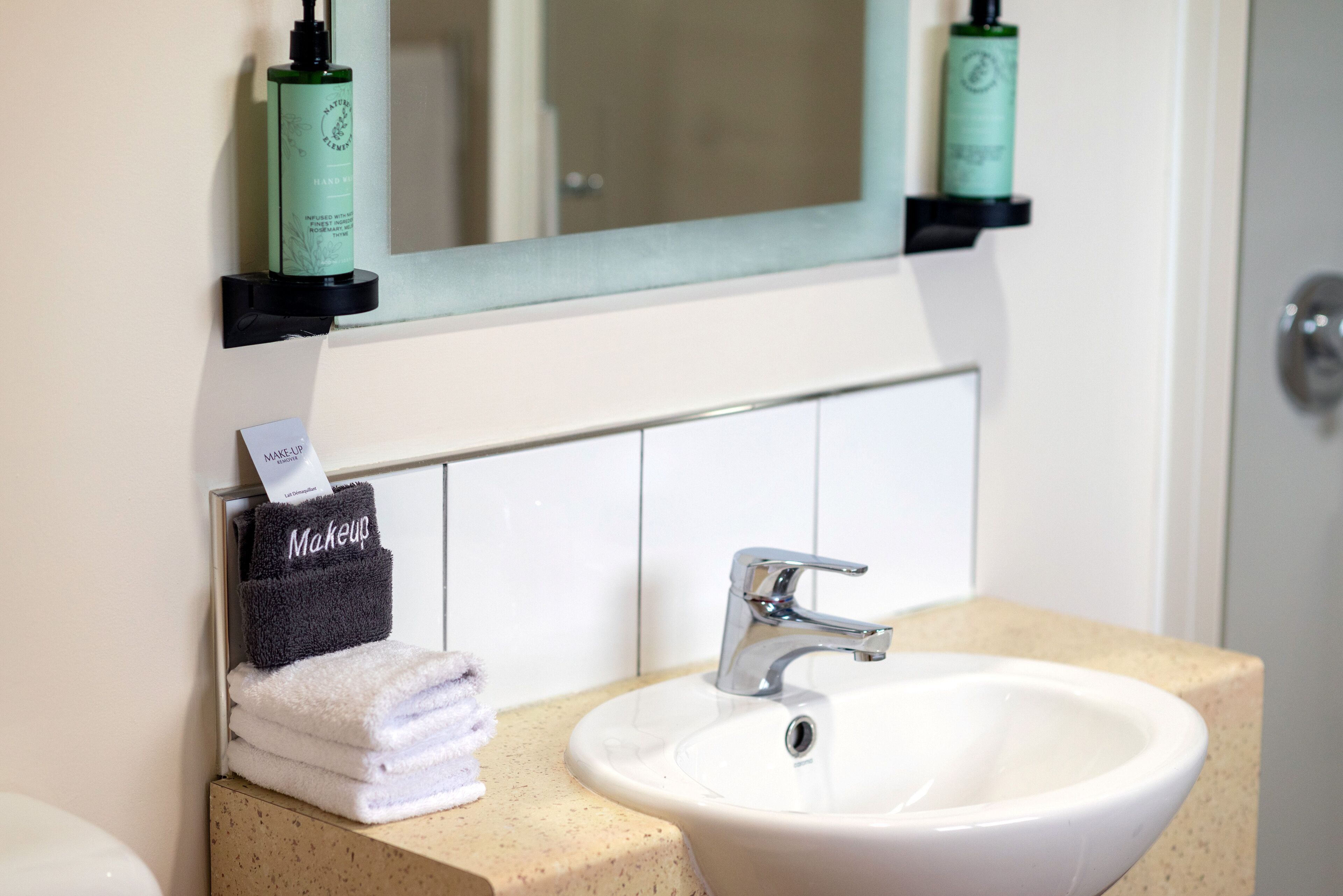 A bathroom with a white sink, a mirror above it, and two shelves holding toiletries.