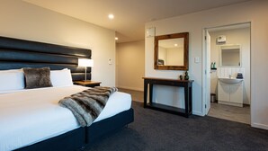 Una habitación de hotel moderna con una cama grande, una mesita de noche, una consola y un espejo, además de un baño con lavamanos y armarios.