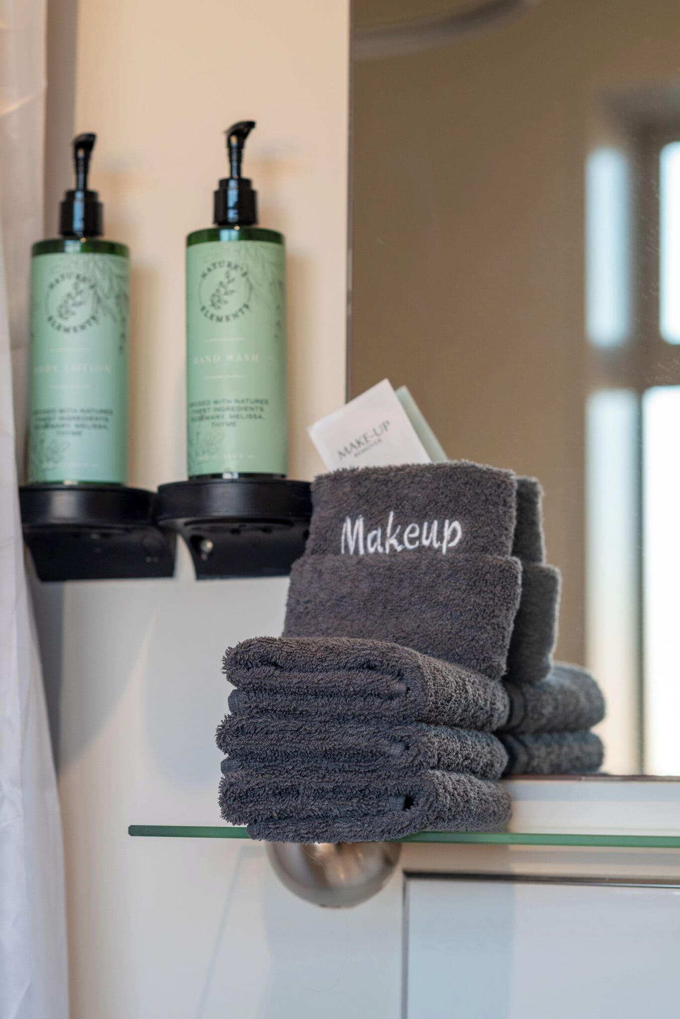 A bathroom with a stack of towels labeled "Makeup" and two green bottles on the wall.