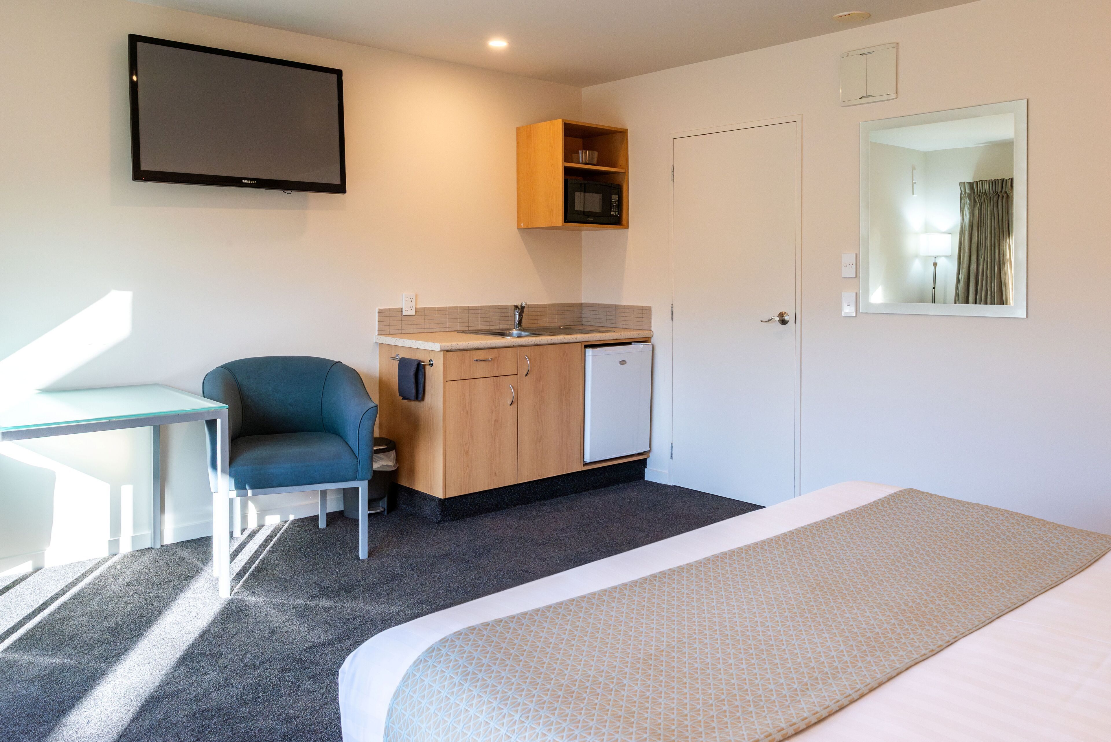 Une chambre d’hôtel équipée d’un lit, d’un bureau, d’une chaise, d’une kitchenette et d’un téléviseur.