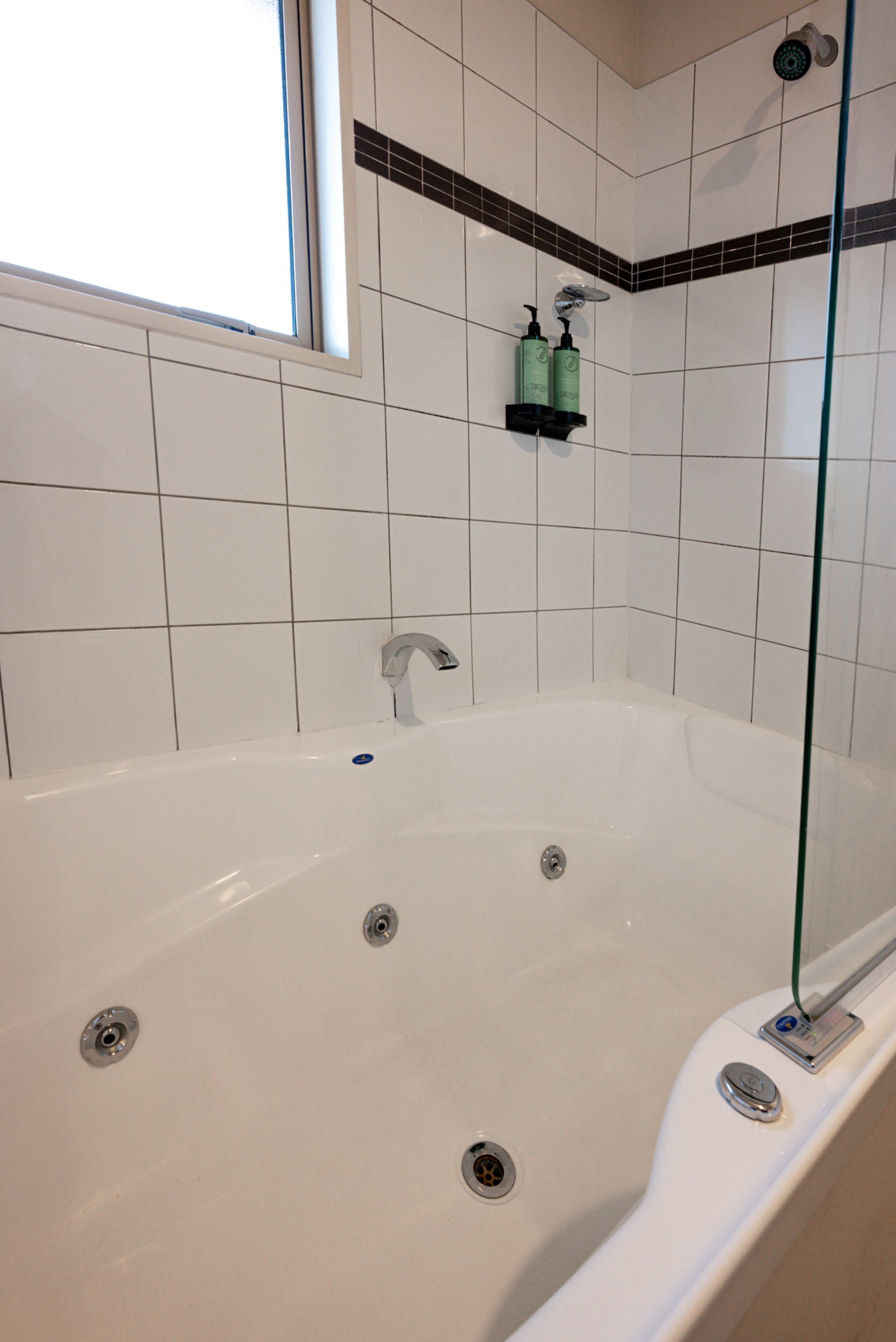 Un baño moderno con una bañera blanca, cabina de ducha con mampara de cristal y ventana que proporciona luz natural.