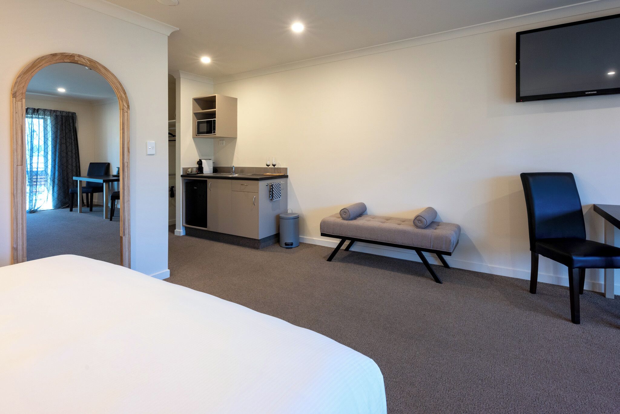 A hotel room with a large bed, a sofa, a chair, a TV, and a kitchenette.