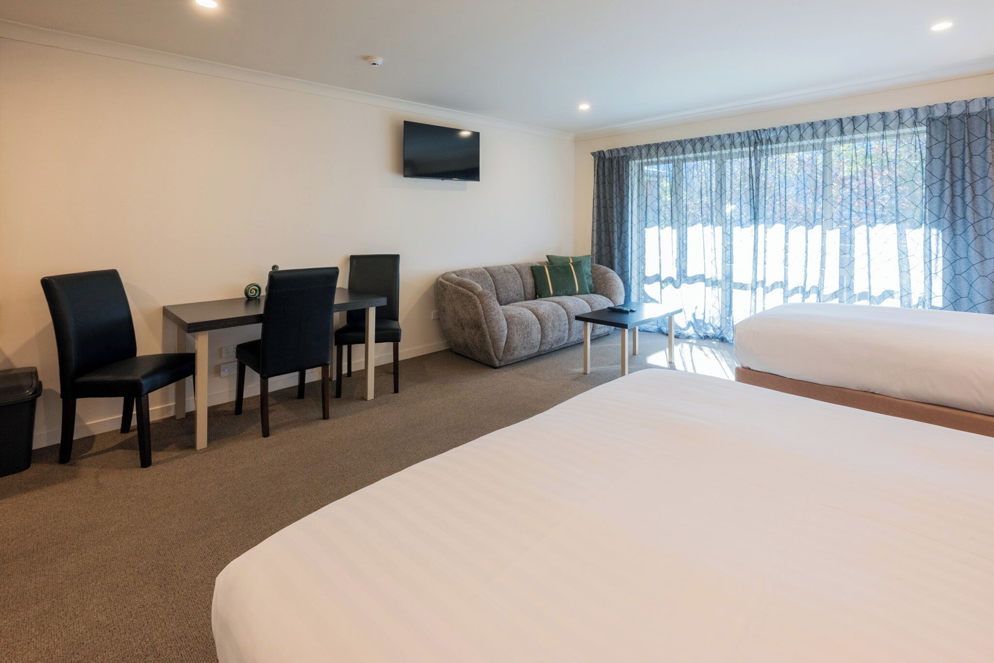 A hotel room with a large bed, a sofa, a desk with chairs, a TV, and a window with curtains.