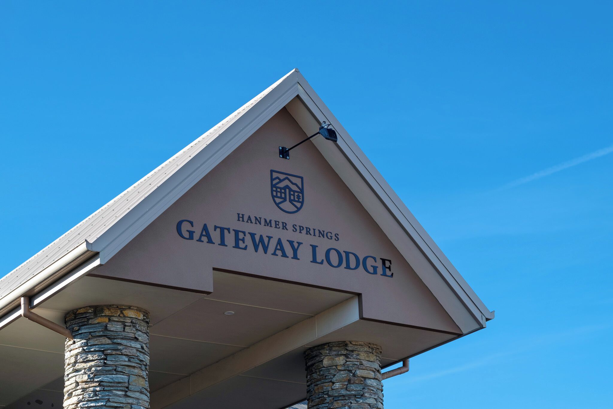 Das äußere Erscheinungsbild des Gateway Lodge in Hanmer Springs, mit einer Steinsäule und wolkenlosem, blauem Himmel.
