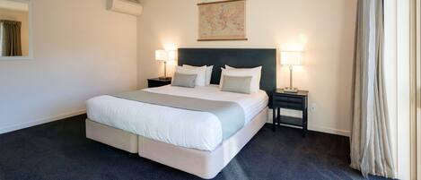 A large bed with a headboard, two bedside tables with lamps, a world map on the wall, and a window with curtains.
