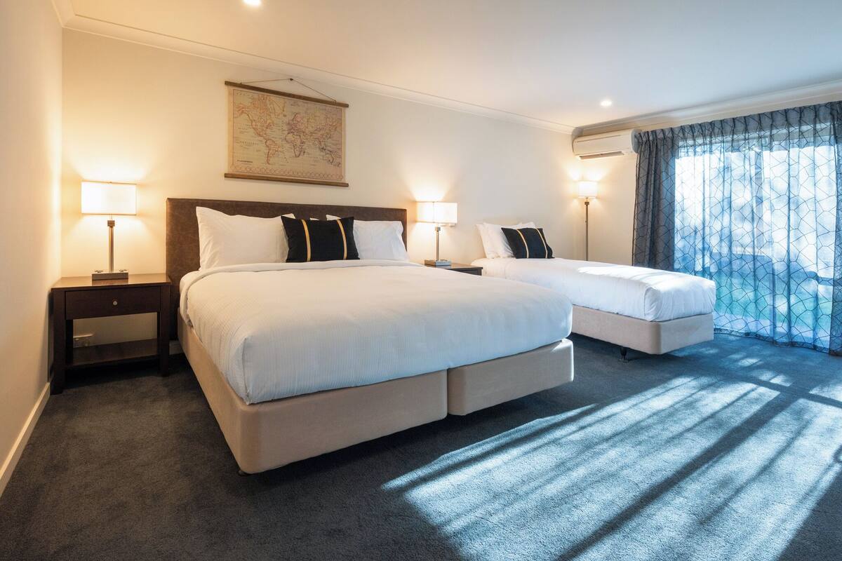 Habitación de hotel con dos camas, un mapa en la pared y una ventana con cortinas.