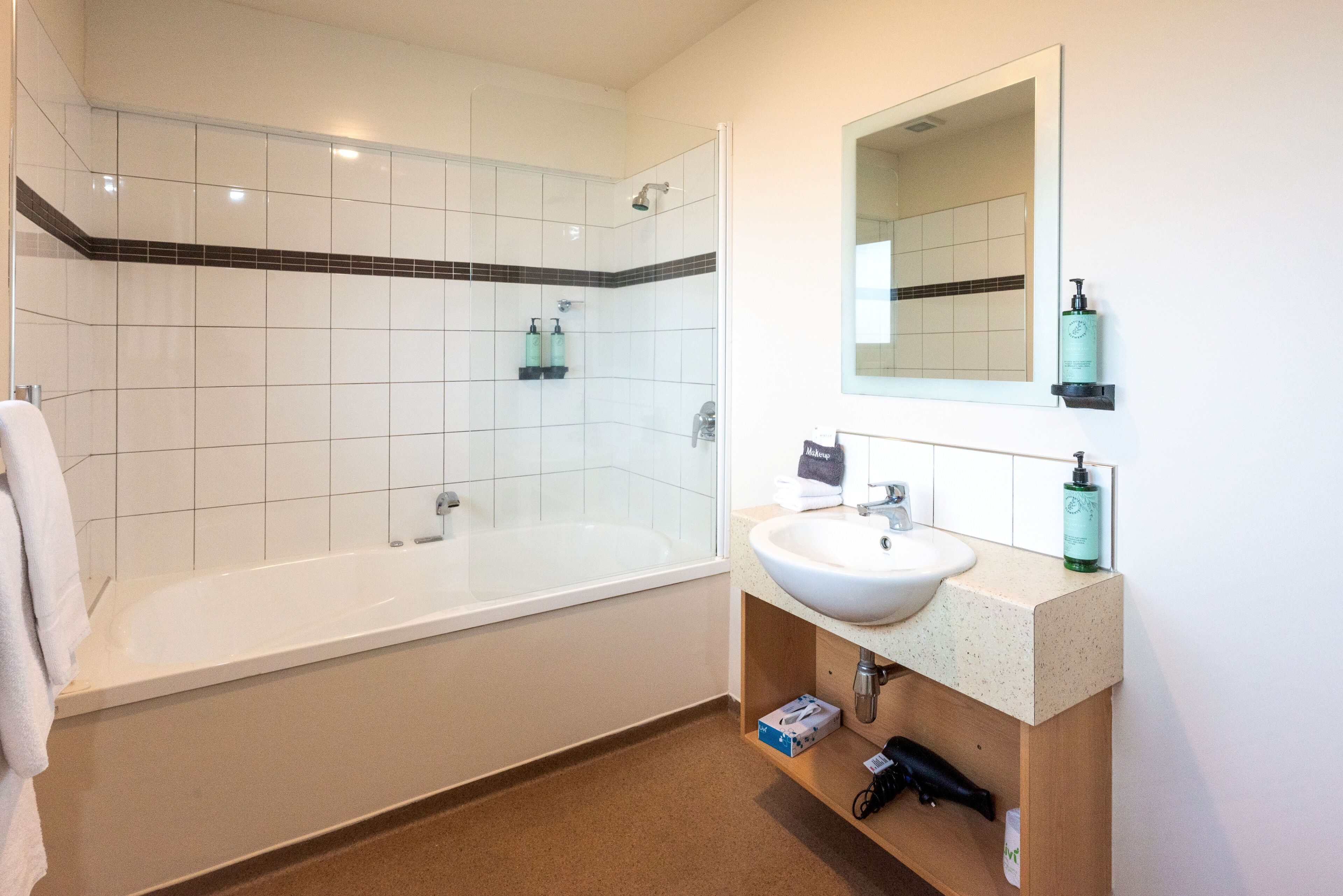 A bathroom with a bathtub, a sink, and a mirror. There are toiletries on the sink and a towel hanging on the wall.