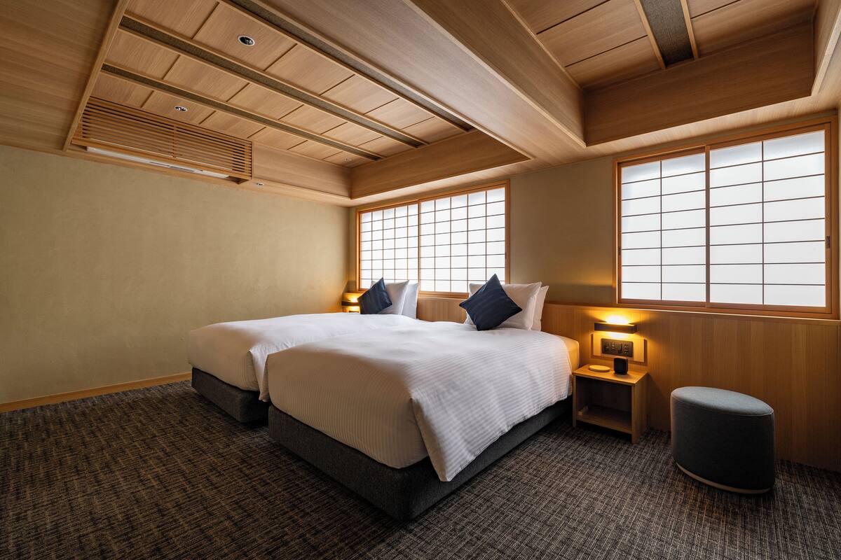 A hotel room with a large bed, two bedside tables, a nightstand, a small ottoman, and a window with a view.