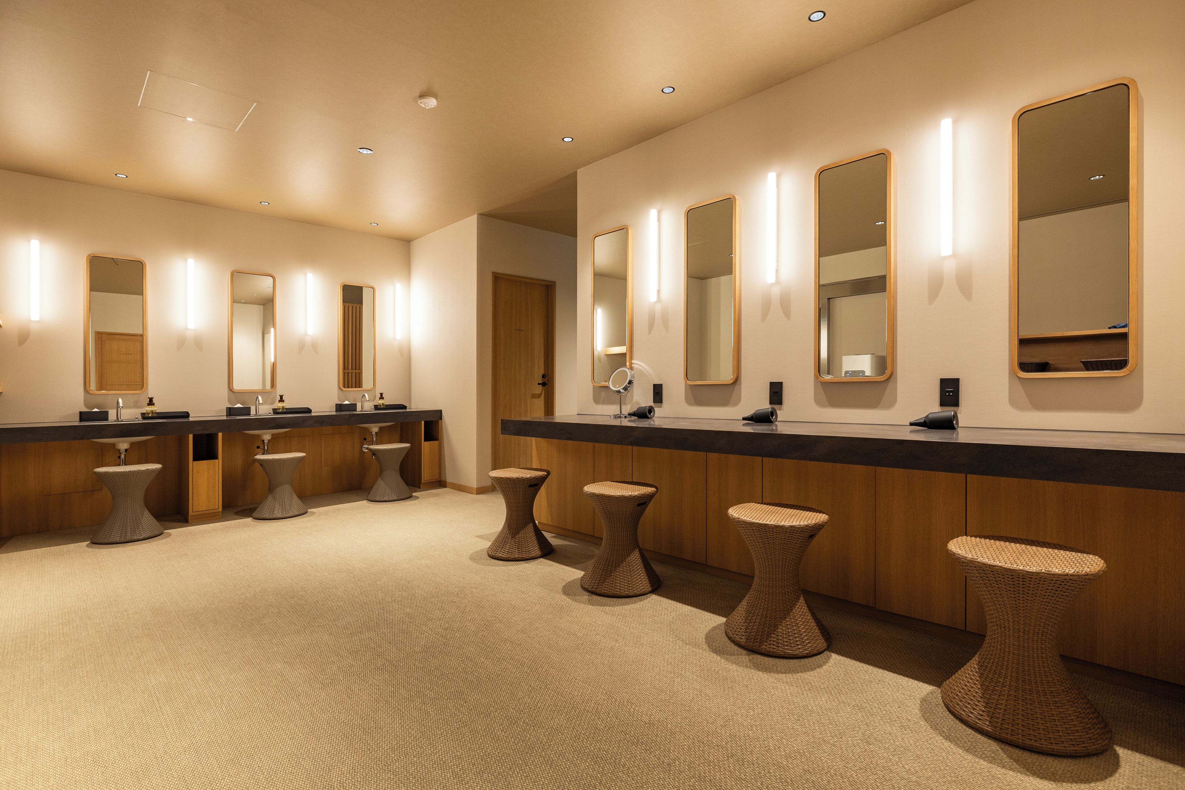 Une salle de bain moderne dotée de plusieurs lavabos, de miroirs et de tabourets en osier.