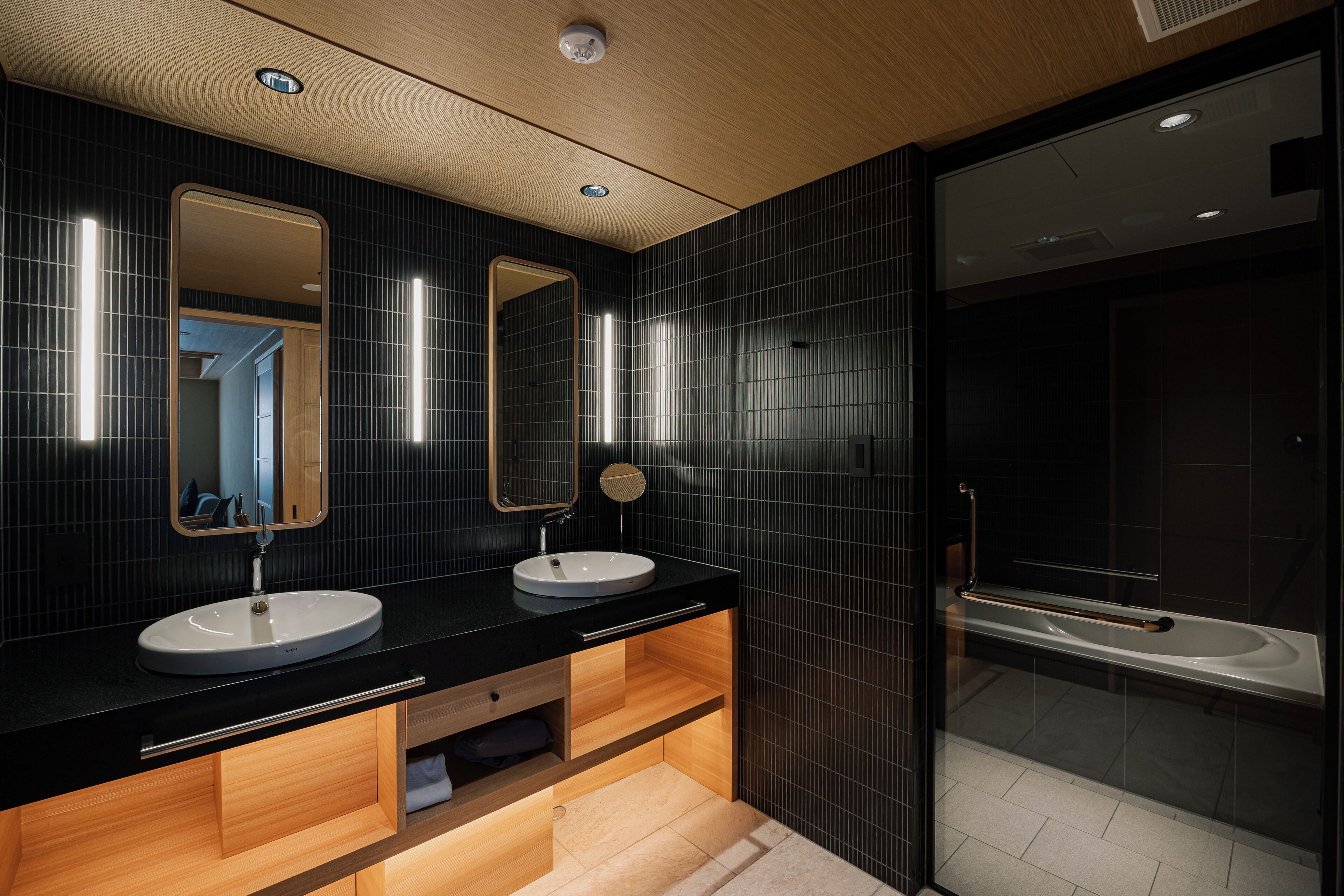 A modern bathroom with two sinks, a large mirror, and a glass-enclosed shower area.