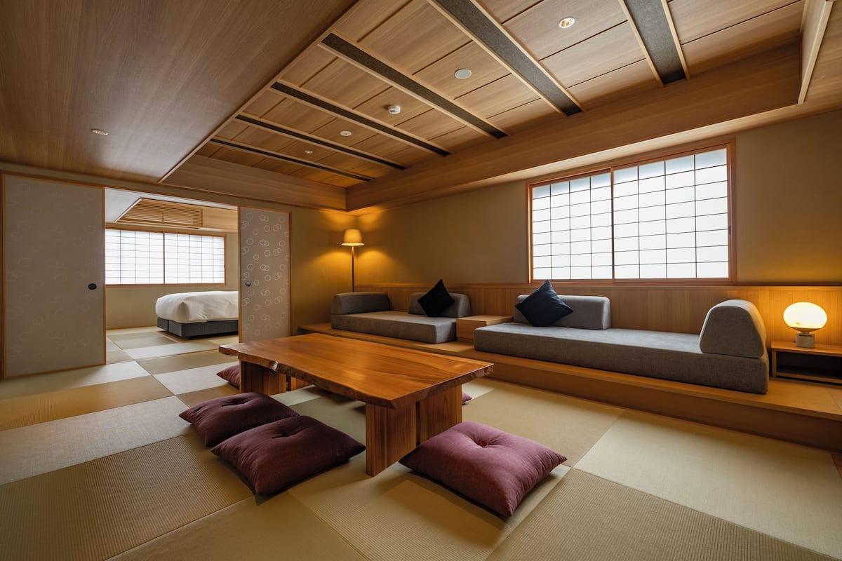 A traditional Japanese-style room with tatami flooring, a low wooden ceiling, and a combination of tatami mats and cushions.