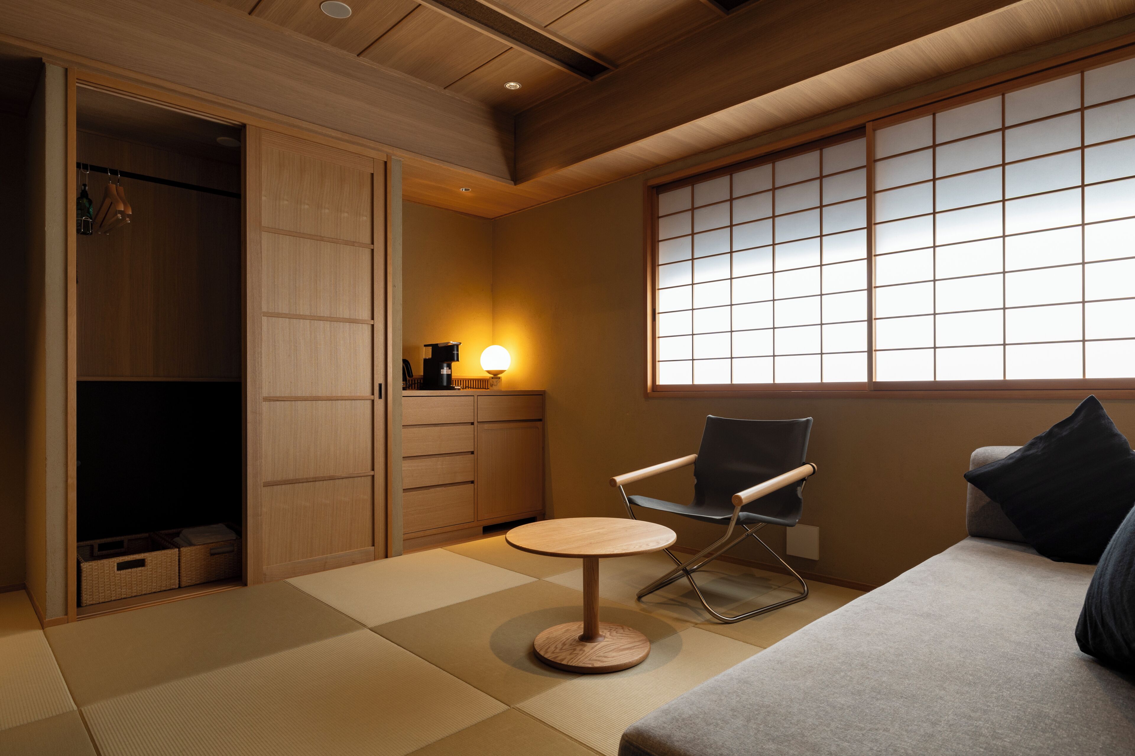 Een kamer met tatami vloer, een lage tafel, een stoel, een bank, een kledingkast en een raam met uitzicht.