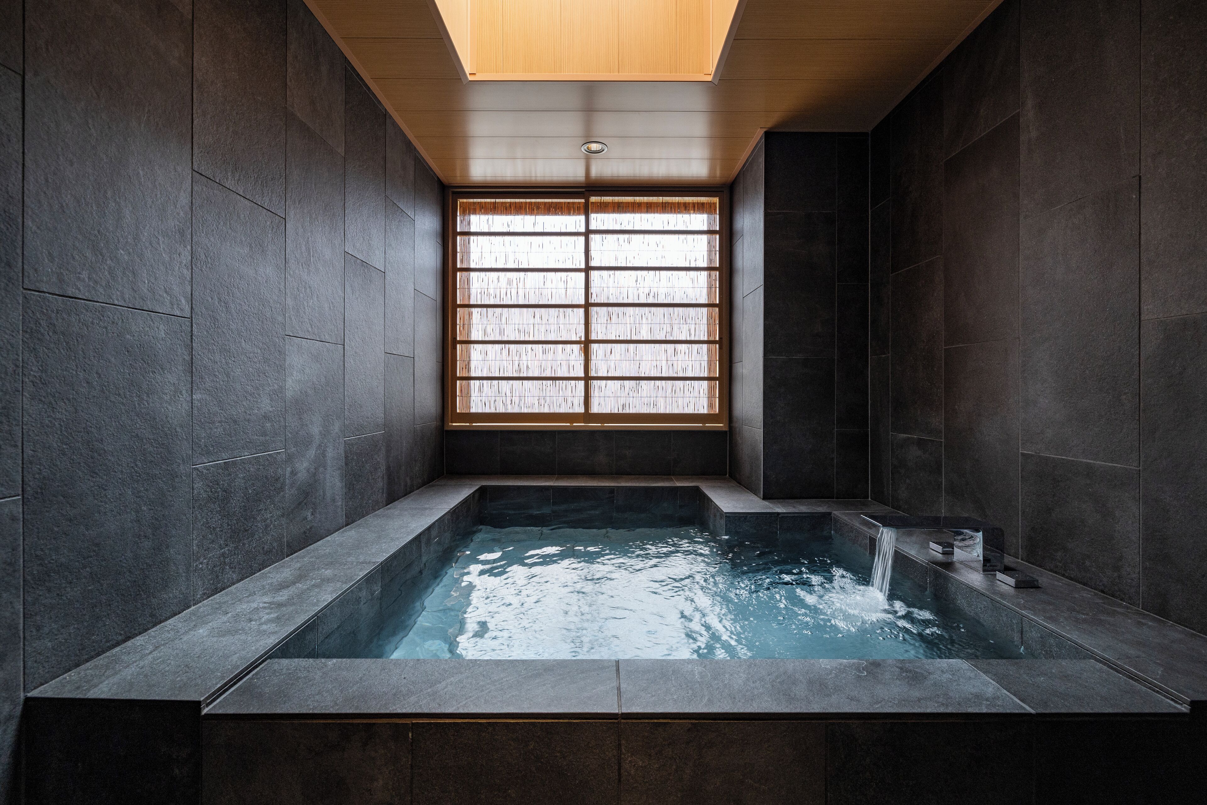 Un spa moderno con un jacuzzi rectangular, paredes de piedra oscura y techo de madera.