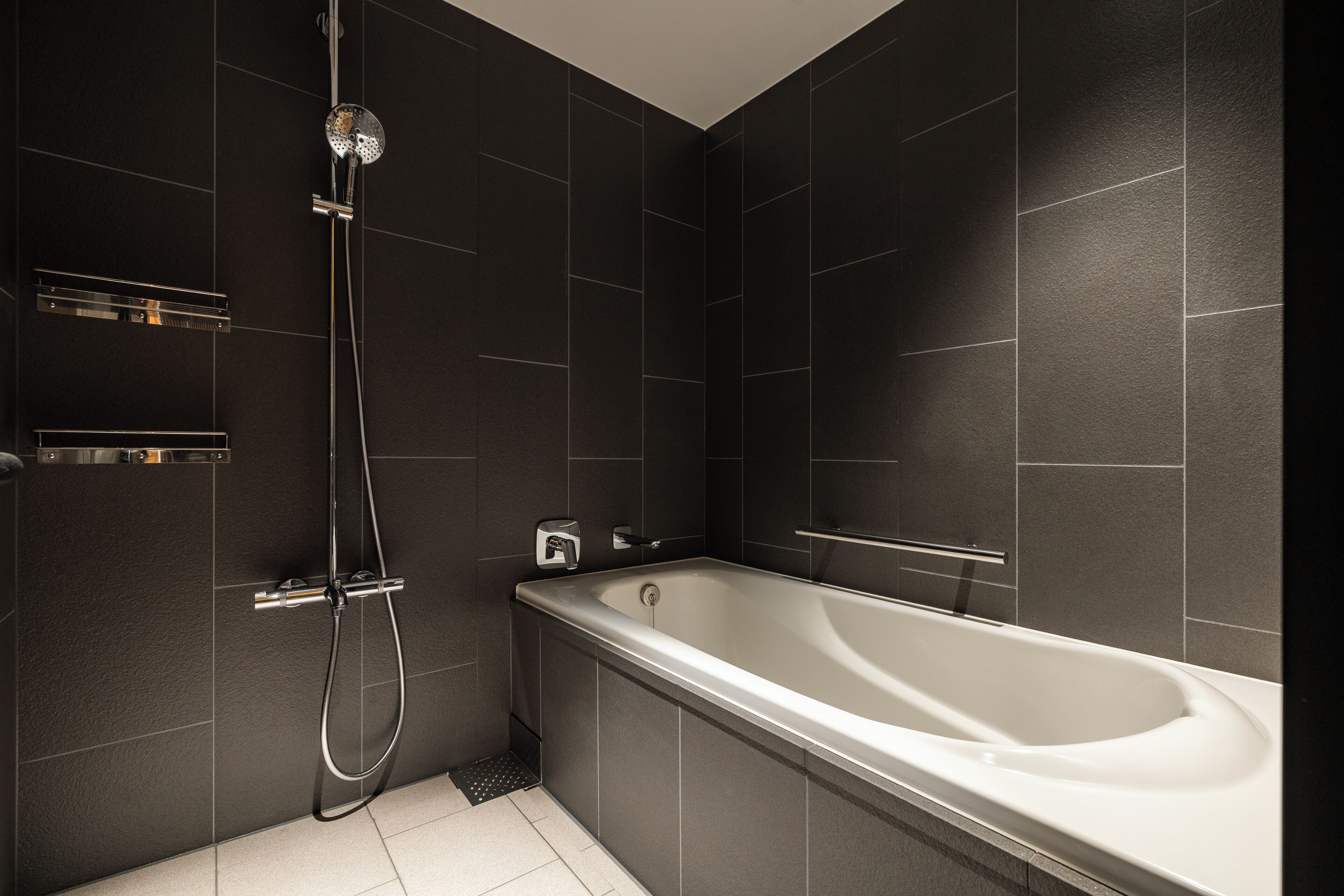 Une salle de bain moderne avec une baignoire, une douche et des murs recouverts de carreaux foncés.