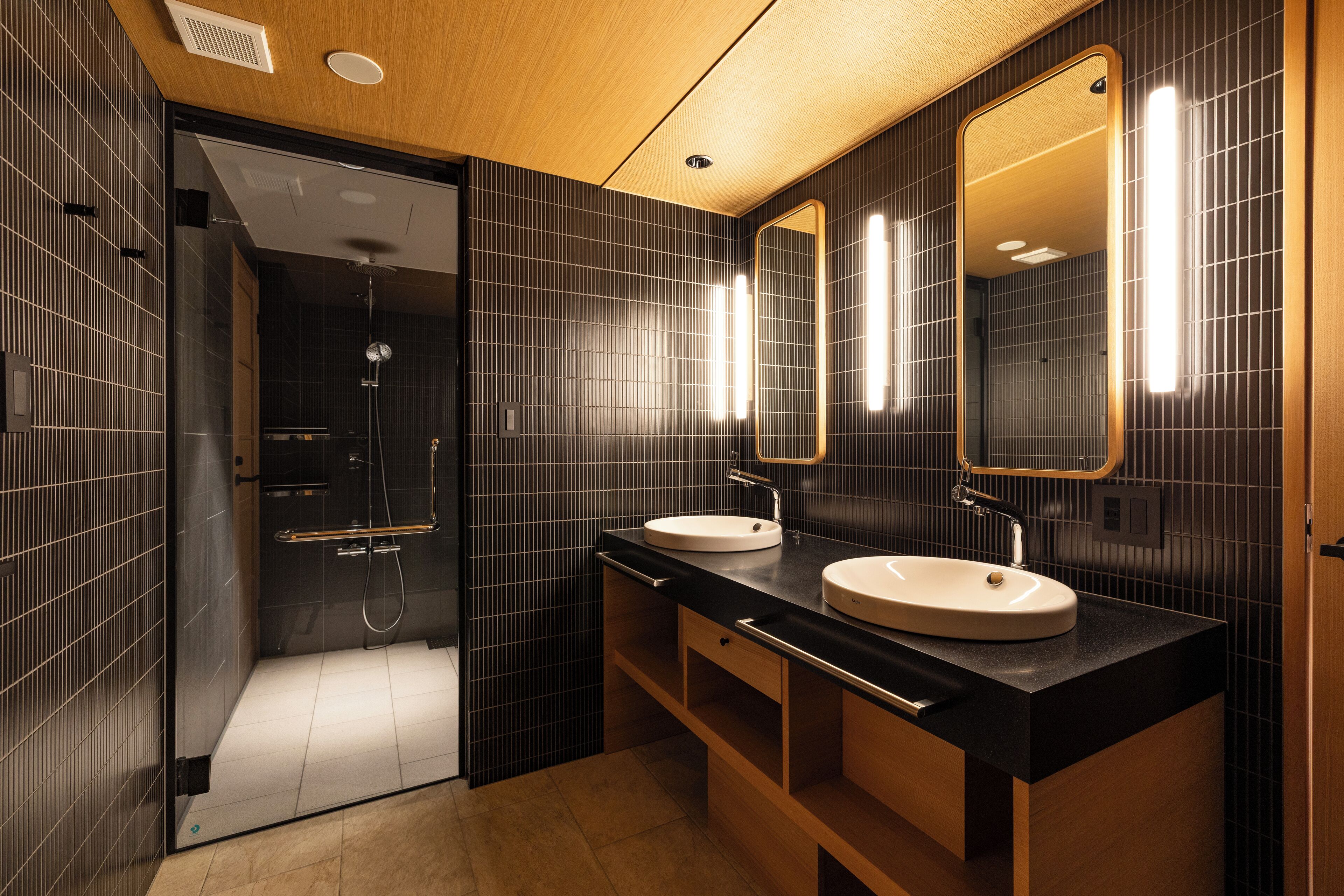 A modern bathroom with two sinks, a large mirror, and a shower area.