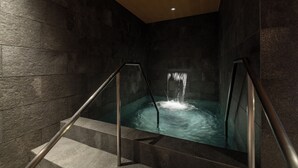 A modern spa area with a stone wall, a hot tub, and metal railings.