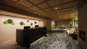 Ein Empfangsbereich mit Empfangsschalter, Wanddekorationen in Kreisform, einer Zimmerpflanze und einer Sitzecke mit Sofa und Bank.