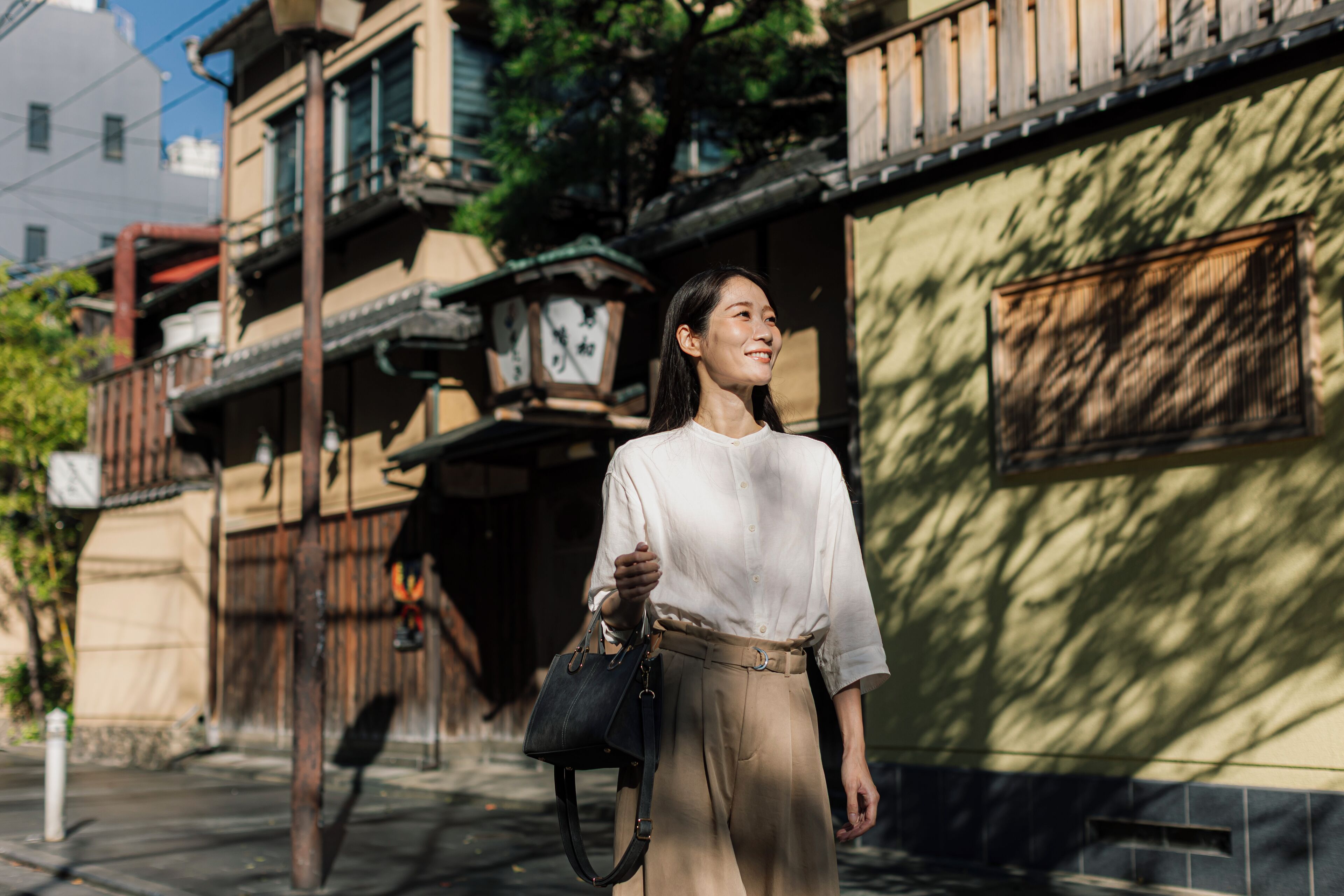 A woman standing on a sidewalk in front of a building with traditional architectural features, including wooden balconies and a clock.