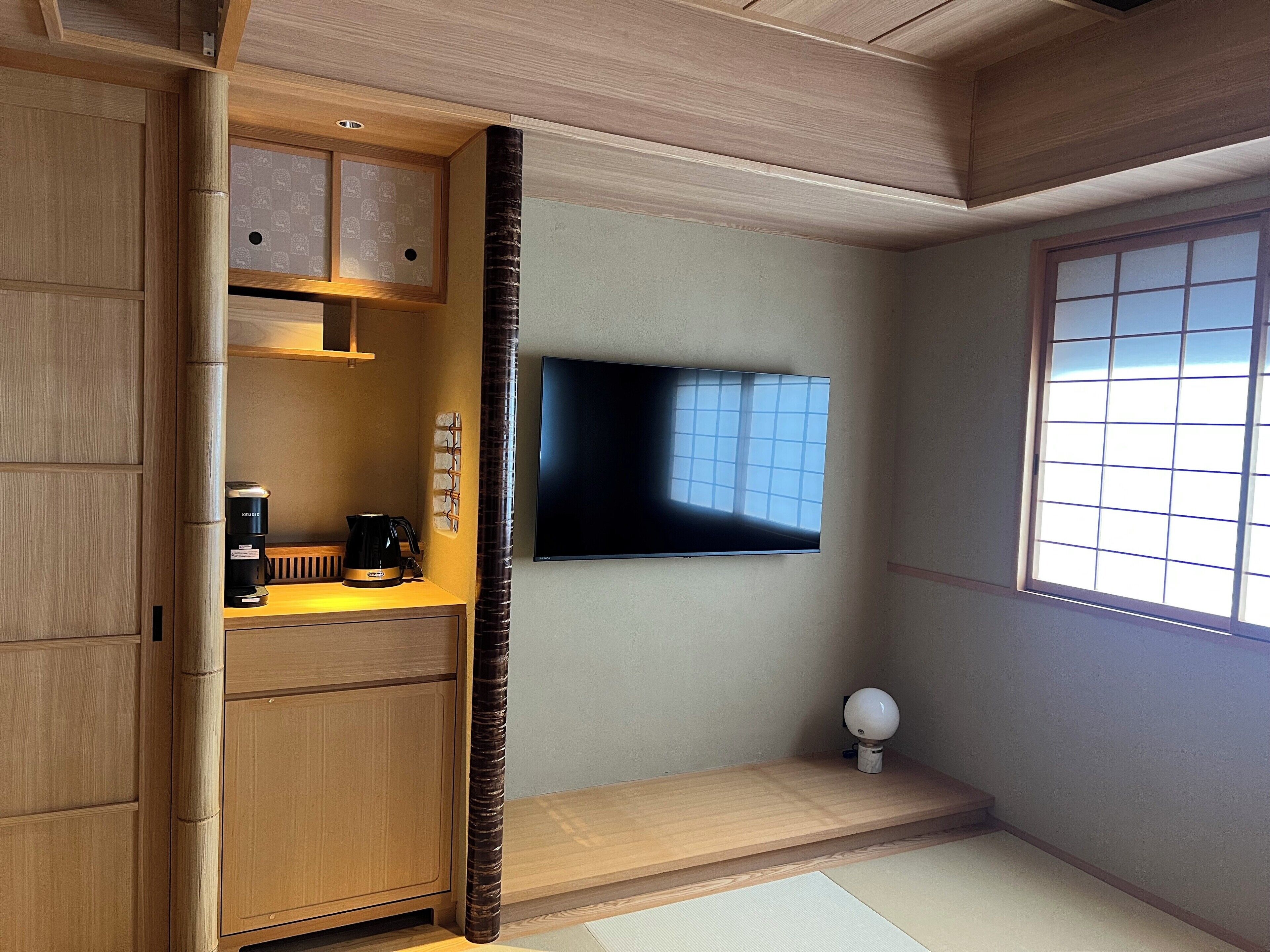 A room with a wooden cabinet, a coffee maker, a flat-screen TV, and a tatami mat floor.
