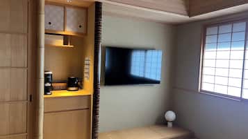 A room with a wooden cabinet, a coffee maker, a flat-screen TV, and a tatami mat floor.