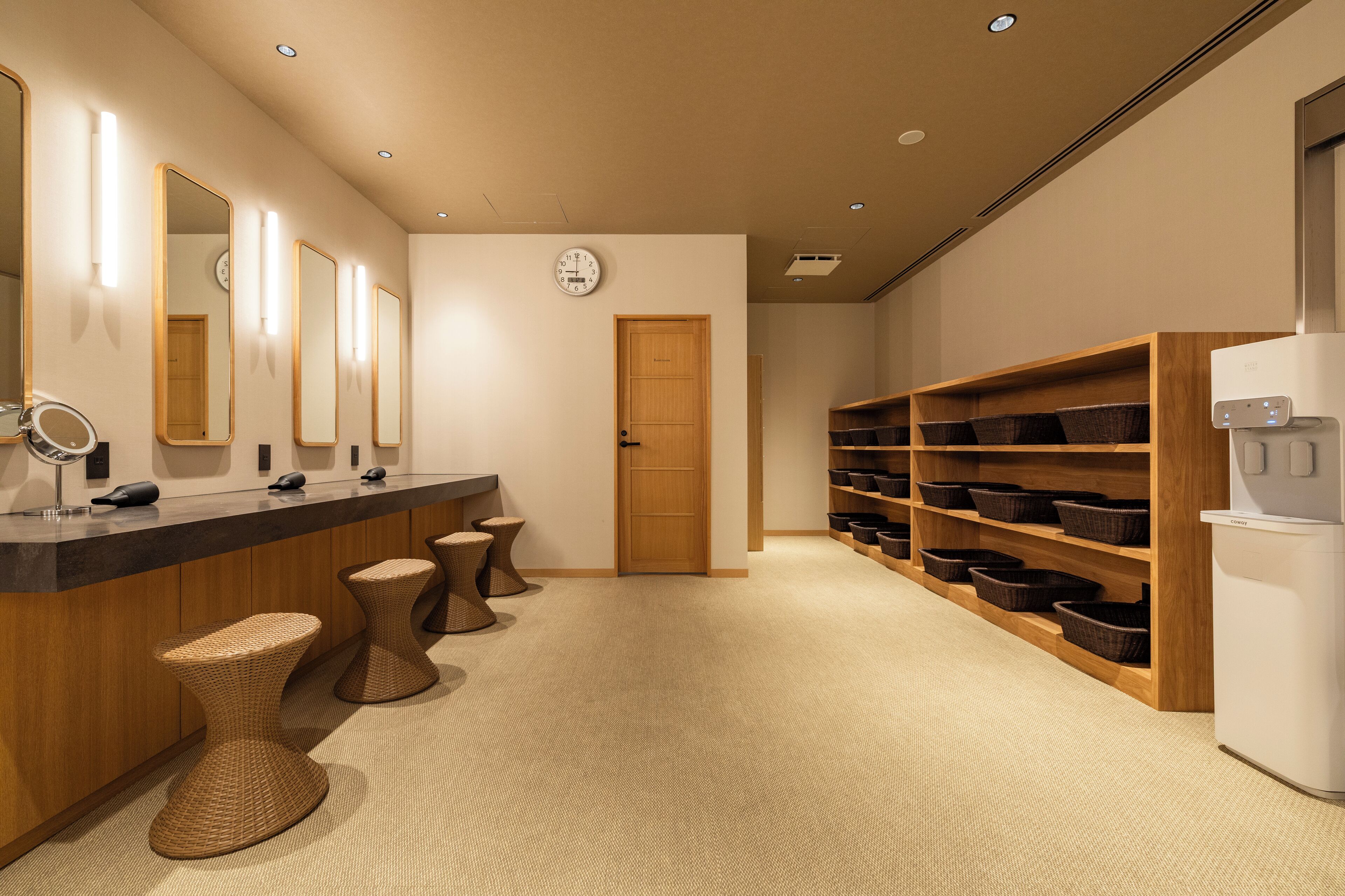 Een moderne badkamer met een houten wastafelmeubel, drie krukken, een spiegel en een plank met manden.