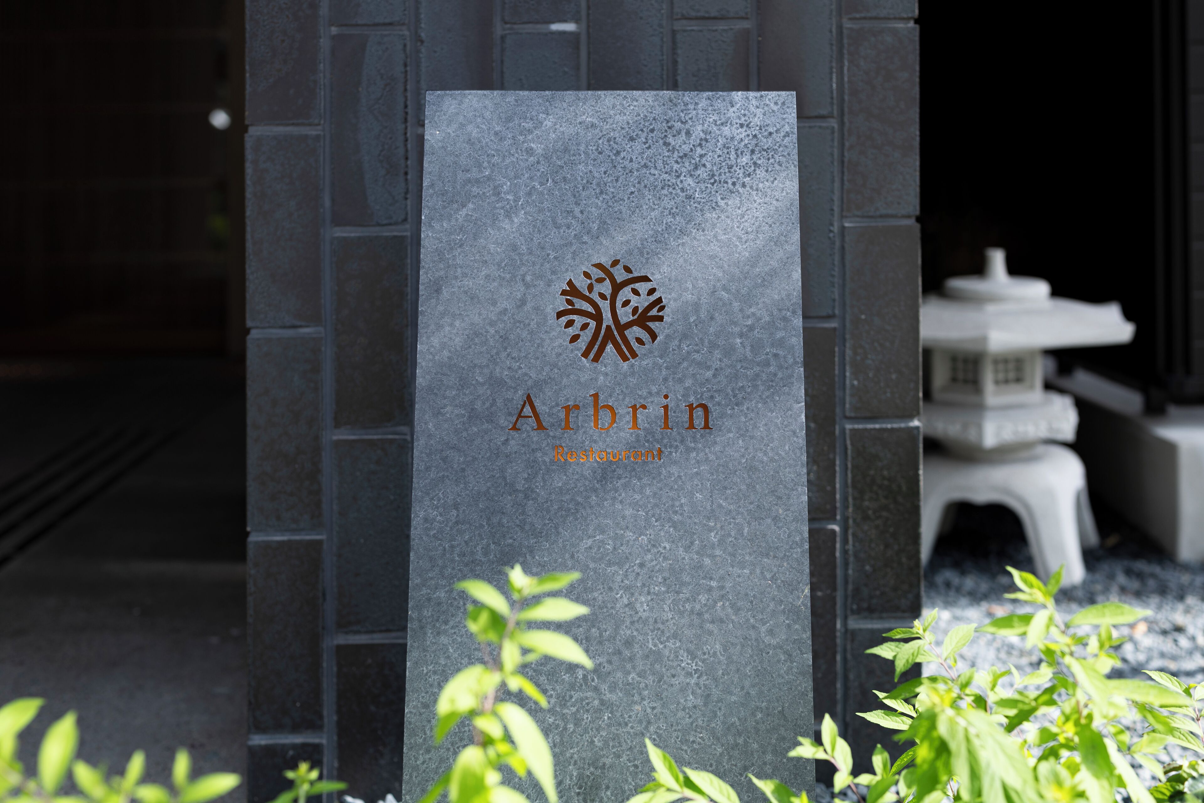 A stone sign with a tree logo and the name 'Arbrin Restaurant' against a dark stone wall.