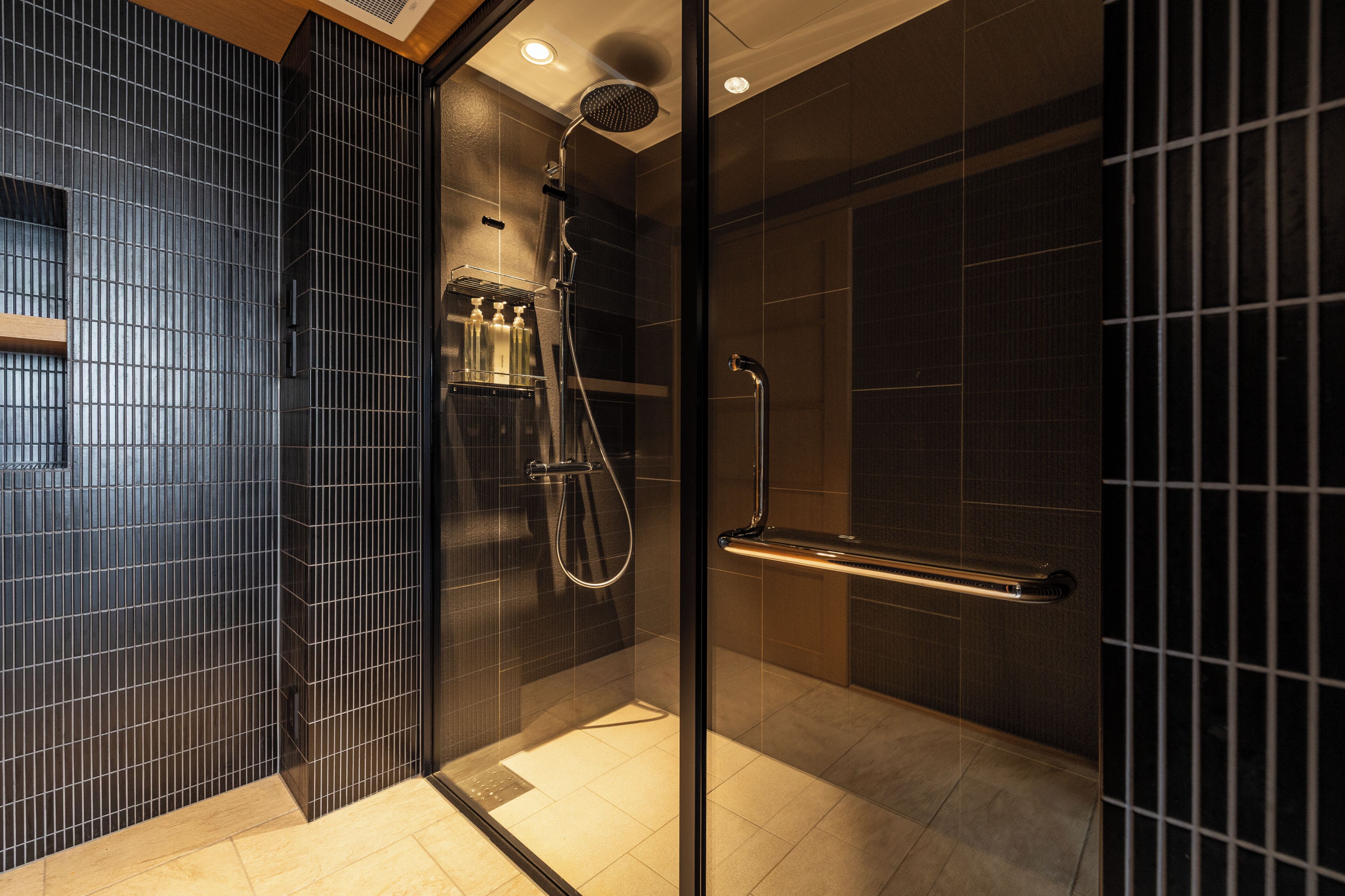 A modern shower area with a glass partition, a handheld showerhead, a wall-mounted towel rack, and a handrail.