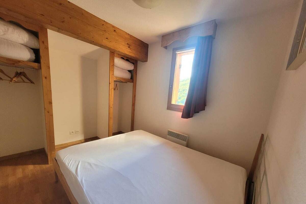 Una habitación pequeña con cama individual, techo de madera, una ventana con cortinas y un radiador en la pared.