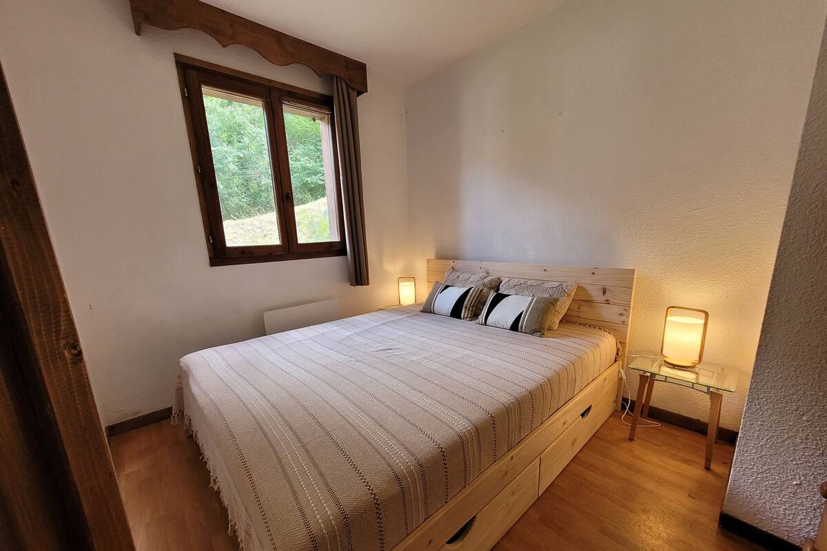 Un dormitorio con cama de madera, una ventana con cortinas y lámparas de noche.