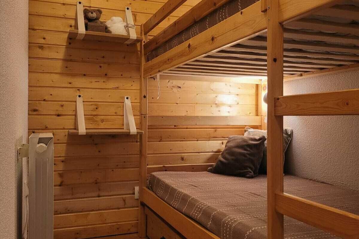 Habitación con literas, paredes de madera, un radiador y una estantería con objetos.
