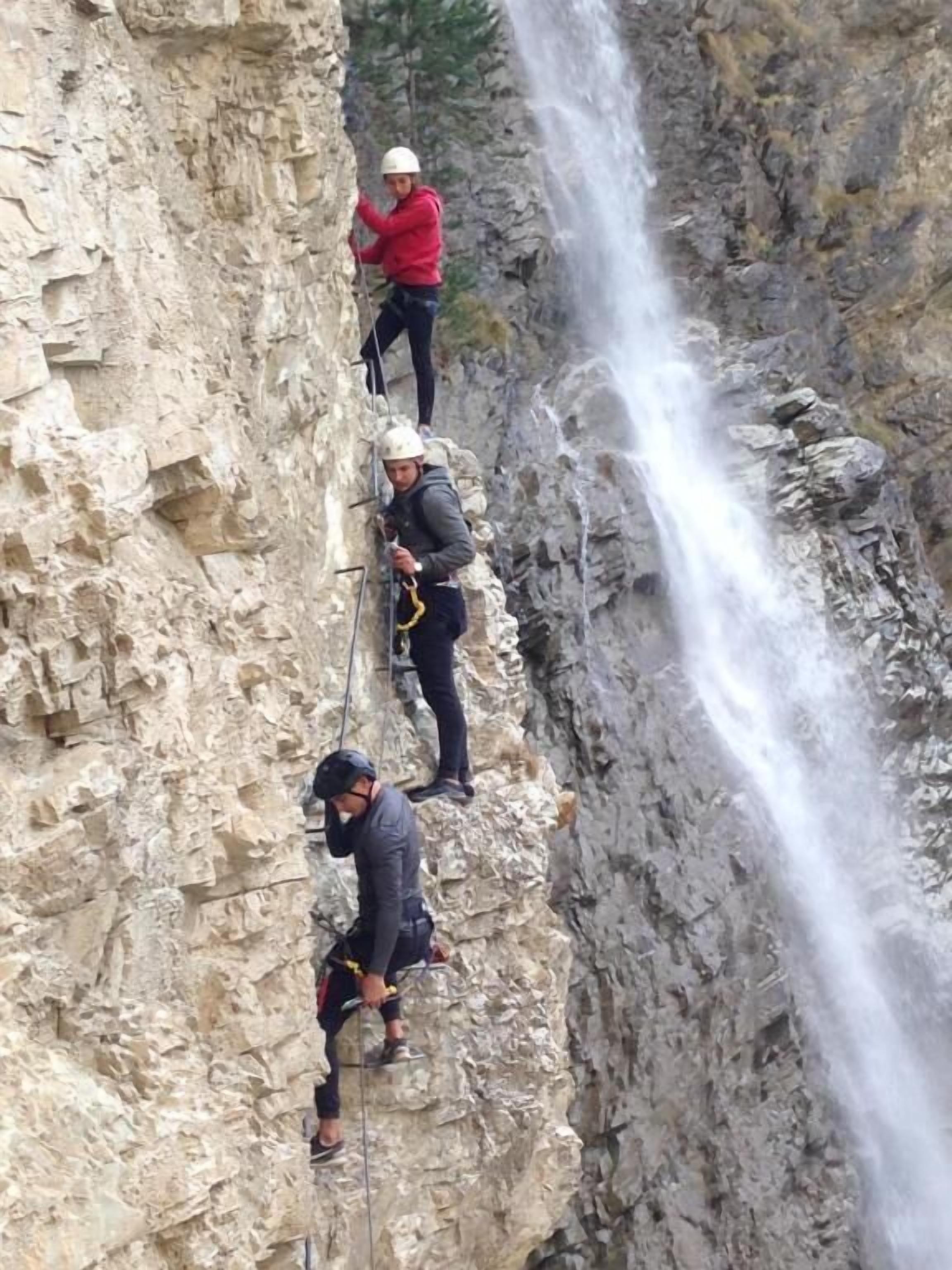 Drei Personen seilen sich an einer felsigen Klippe ab, im Hintergrund ein Wasserfall.
