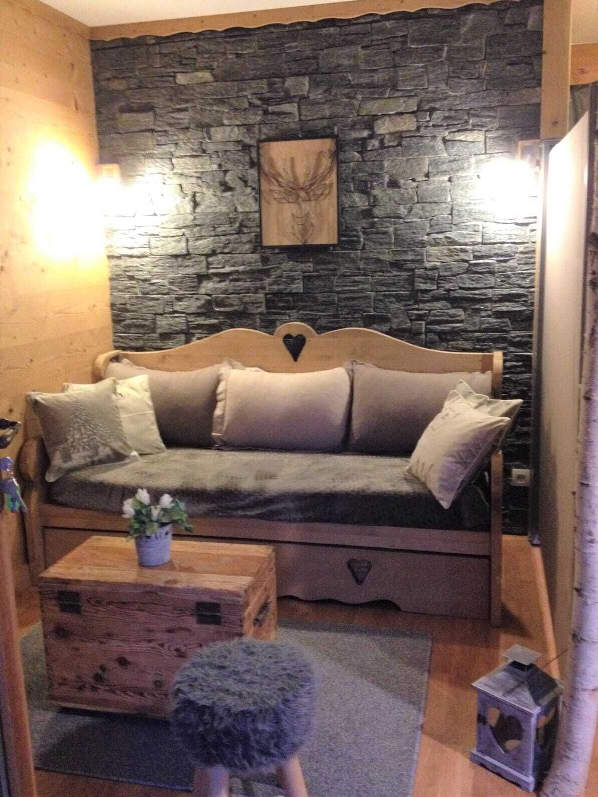 A cozy room with a stone wall, a wooden sofa with cushions, a small wooden table with a plant, and a decorative item on the wall.