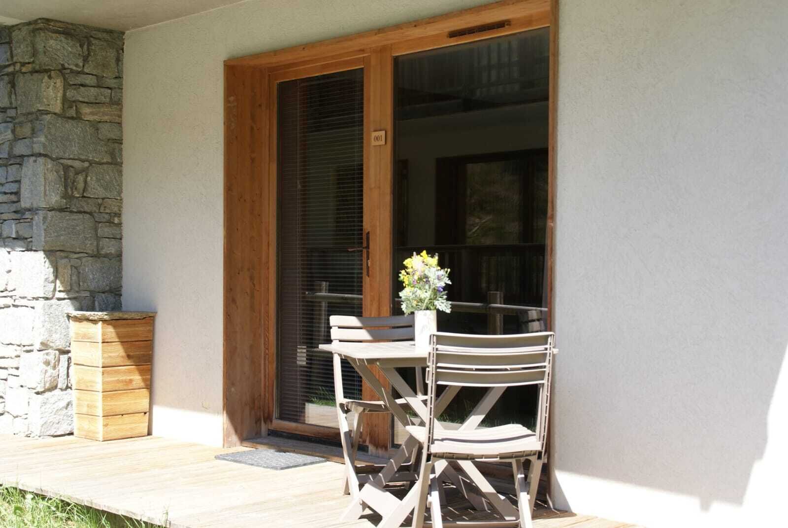 Une terrasse avec une table et des chaises en bois, un mur en pierre et une porte-fenêtre coulissante.
