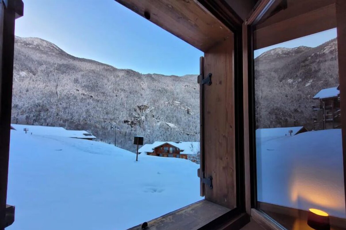 Een houten raamkozijn met uitzicht op een besneeuwd landschap en een blokhut.