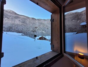 Een houten raamkozijn met uitzicht op een besneeuwd landschap en een blokhut.